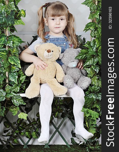 Tired little girl in denim jumpsuit sits on swing