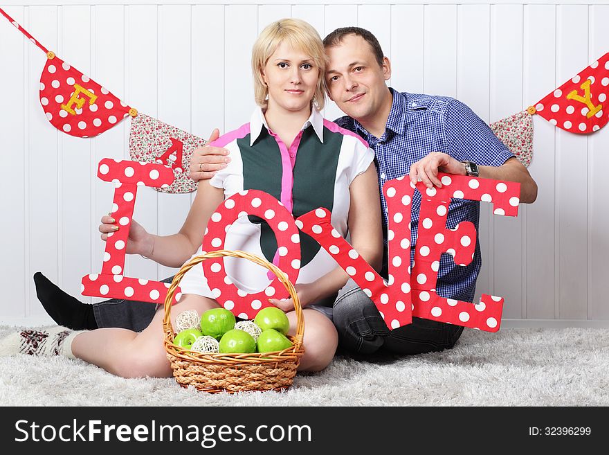 Happy pregnant wife and husband sit on carpet and hold letters L O V E.