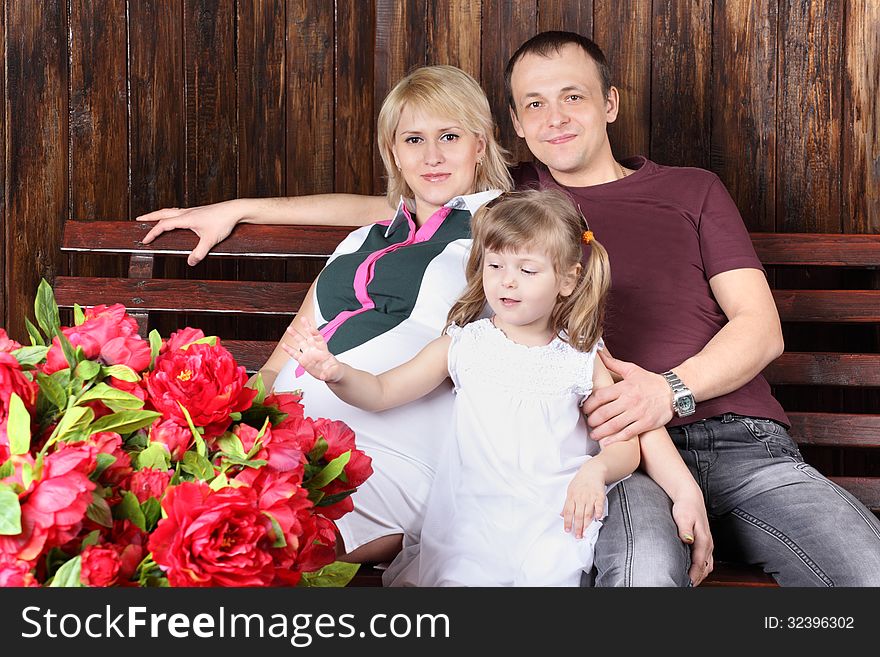 Father, pregnant mother and little daughter sit on bench next to large bouquet of flowers. Father, pregnant mother and little daughter sit on bench next to large bouquet of flowers.