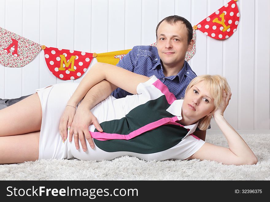 Happy pregnant wife and husband lie on carpet and hold belly.