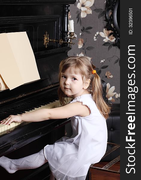 Little beautiful girl in white dress sits at black piano with music. Little beautiful girl in white dress sits at black piano with music.