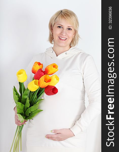 Happy pregnant woman in white with bouquet of tulips on white background.