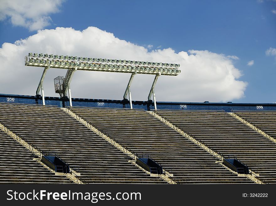 Stadium lights above empty seats with a cloud in the background. Stadium lights above empty seats with a cloud in the background.