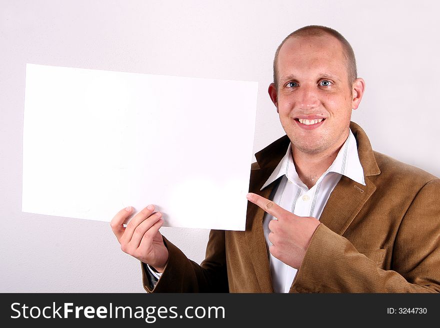 A young businessman is amiling and holds a sign and points at it! White sign to write on!. A young businessman is amiling and holds a sign and points at it! White sign to write on!