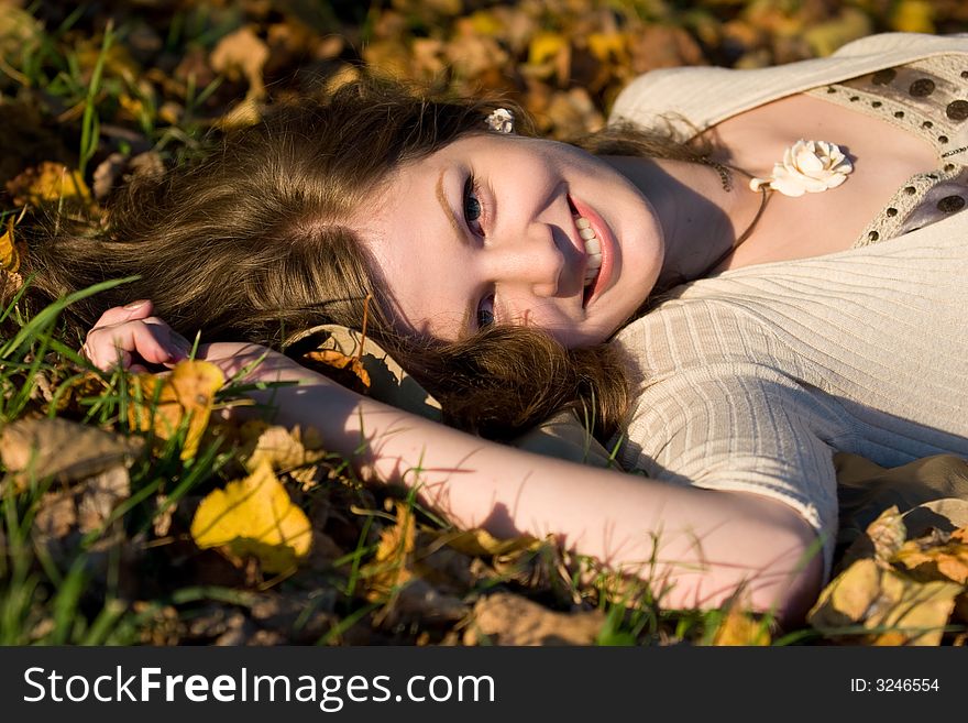 Laughing Girl lying in autumn leaves on sunset time. Laughing Girl lying in autumn leaves on sunset time