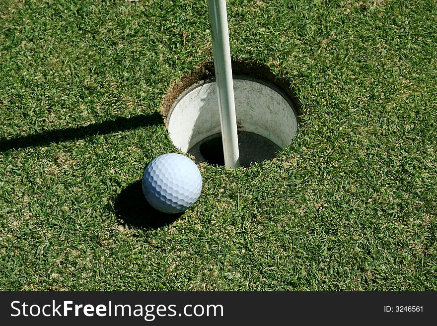 A Golf Ball on green near hole with flag pole