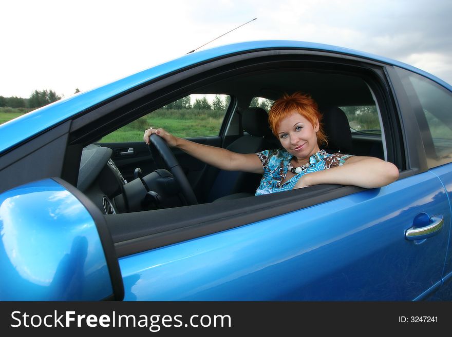 Young red-haired woman is siting in a car. Woman is happy. Young red-haired woman is siting in a car. Woman is happy