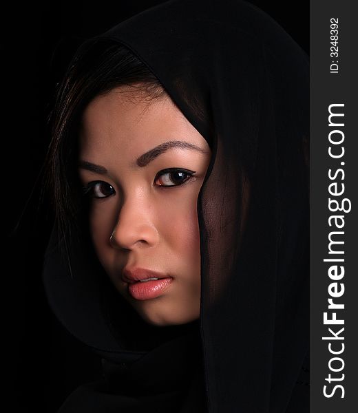 A Beautiful Asian shy looking girl over black with a black scarf over her head. A Beautiful Asian shy looking girl over black with a black scarf over her head