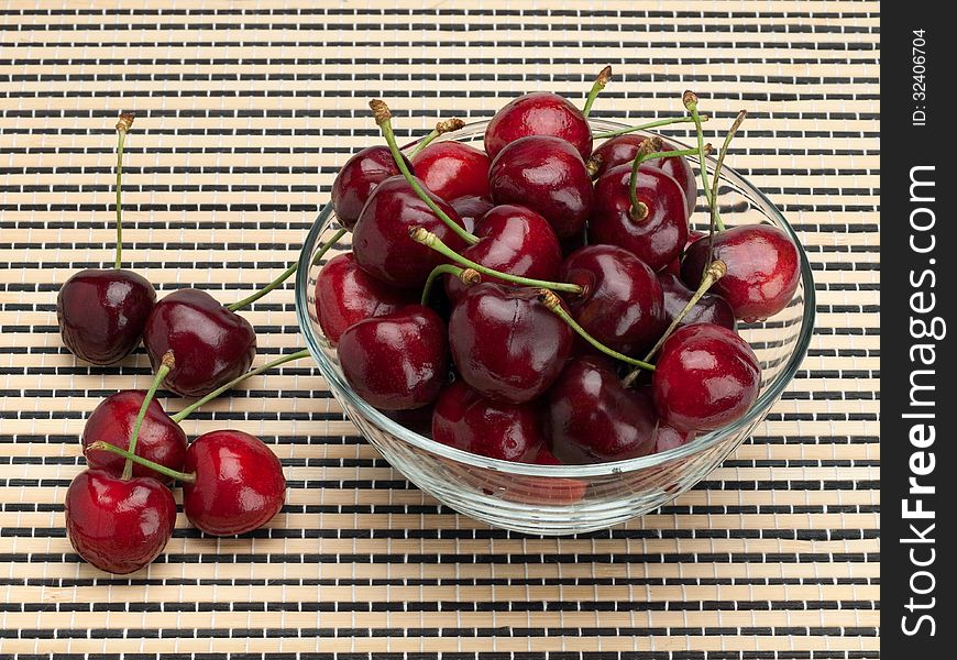 Sweet cherry in a glass vase on a wattled mat