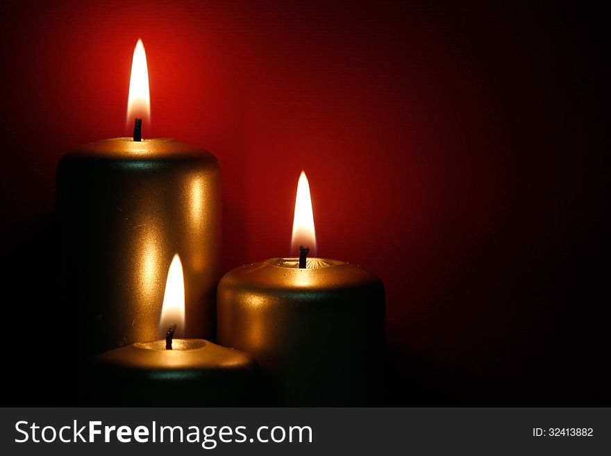 Three burning gold candles on the red background. Three burning gold candles on the red background