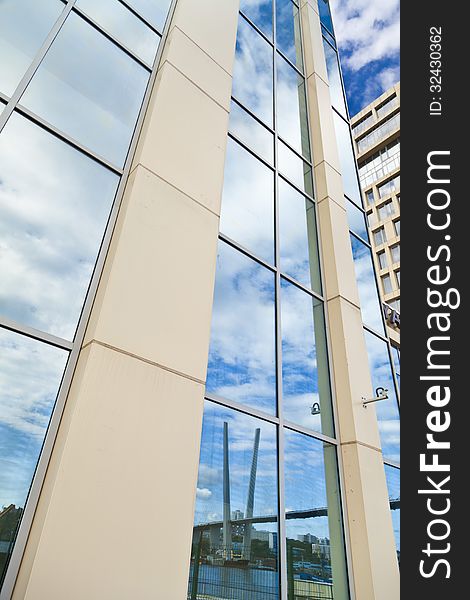 In windows of the modern building are reflected the blue sky and clouds