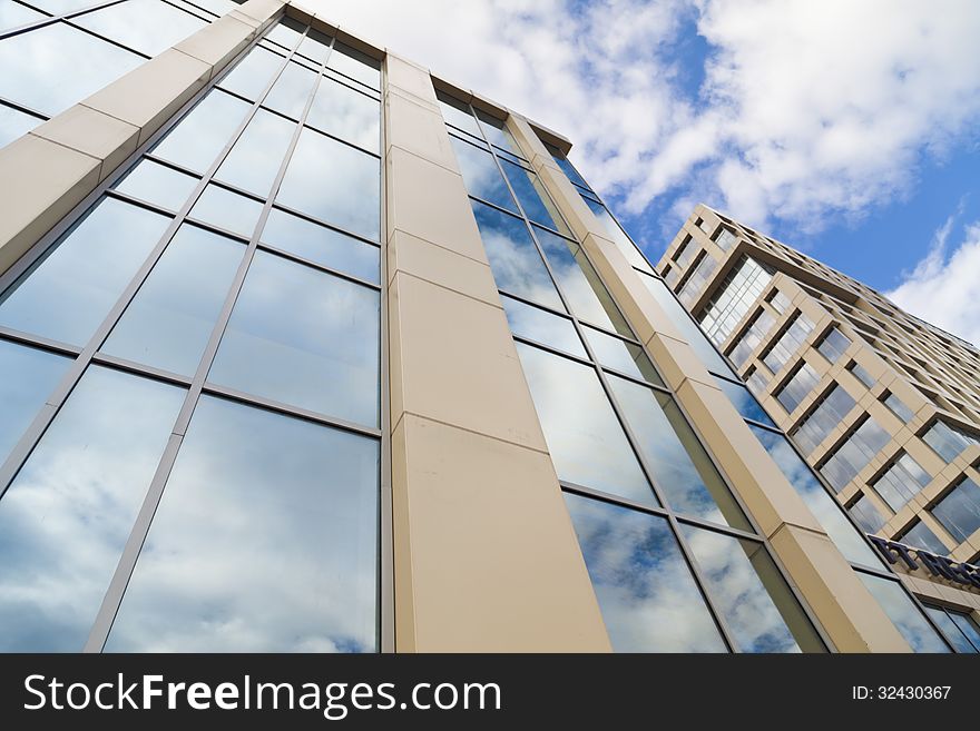 In windows of the modern building are reflected the blue sky and clouds