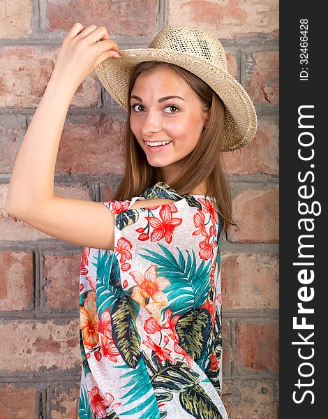 The beautiful girl in a summer hat against a brick wall. Studio portrait. The beautiful girl in a summer hat against a brick wall. Studio portrait