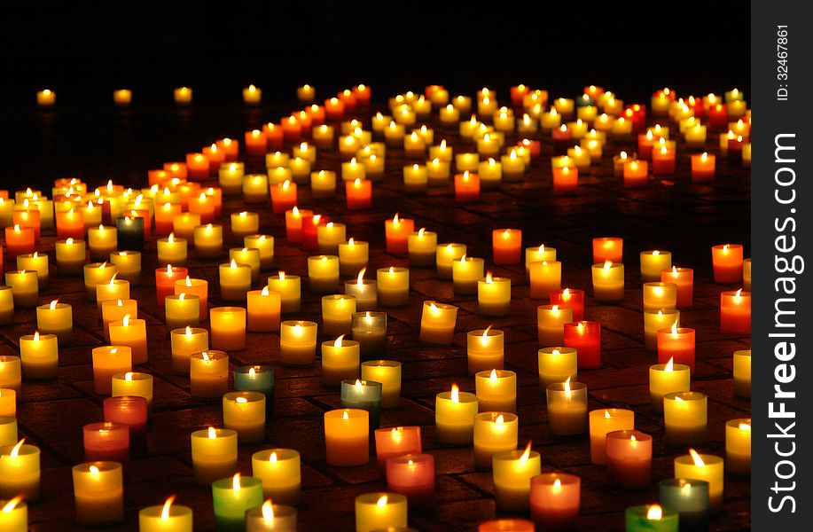 Multicolored lighted candles on the sidewalk at night with local focus. Multicolored lighted candles on the sidewalk at night with local focus