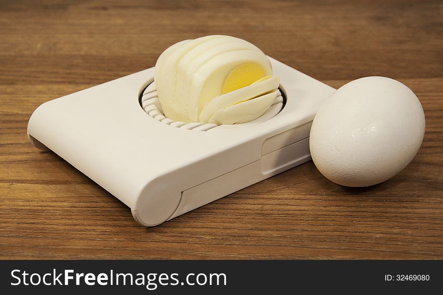 Egg next to boiled egg in egg slicer against a brown wood grained background. Egg next to boiled egg in egg slicer against a brown wood grained background