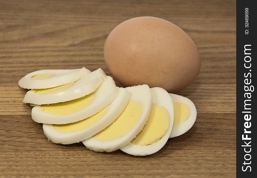 Brown egg and boiled egg slices against a brown wood grained background. Brown egg and boiled egg slices against a brown wood grained background