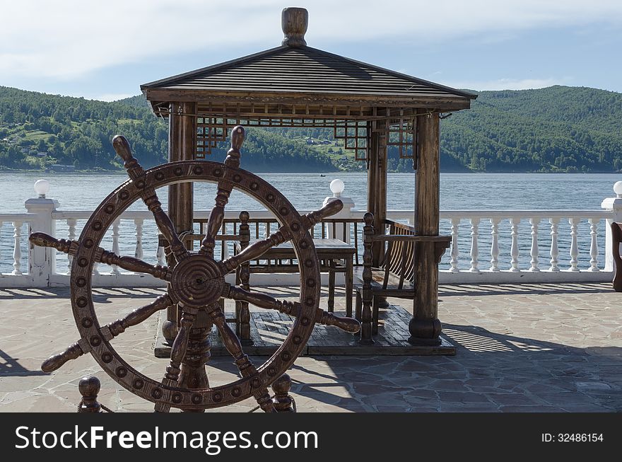 Wooden arbor with table and decorative helm on the Angara river shore