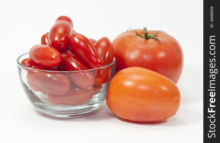 Three types of red tomatoes and a glass bowl against a white background. Three types of red tomatoes and a glass bowl against a white background