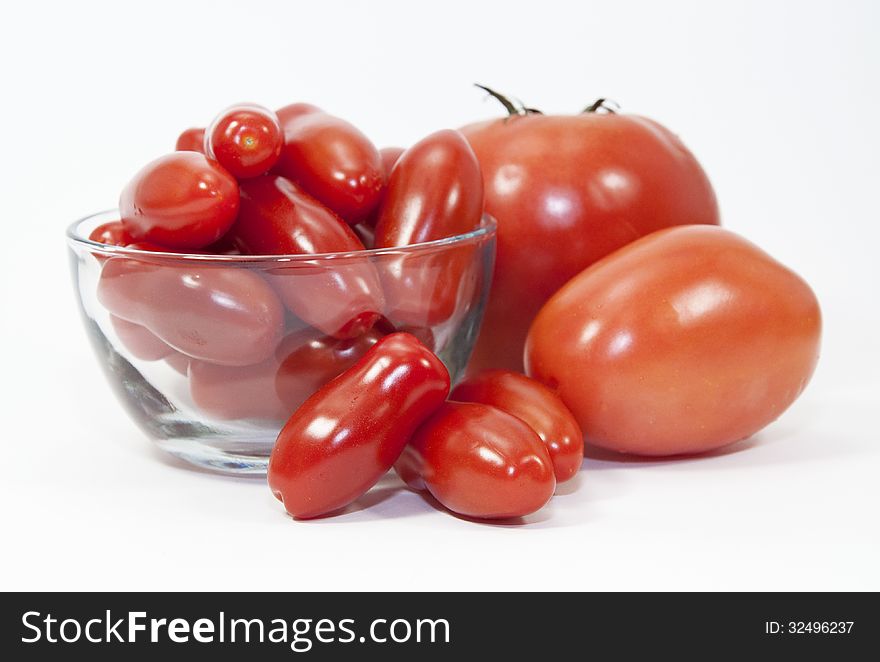 Three types and sizes of red tomatoes and a clear glass bowl against a white background. Three types and sizes of red tomatoes and a clear glass bowl against a white background