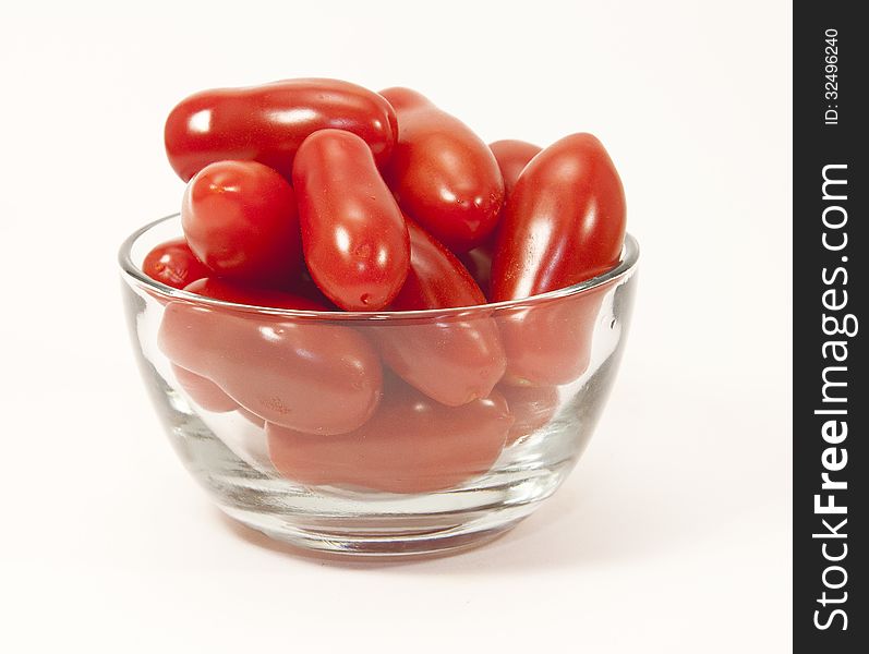 Mini red tomatoes in a clear glass bowl against a white background. Mini red tomatoes in a clear glass bowl against a white background