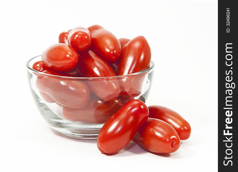 Mini red tomatoes in and next to a glass bowl against a white background. Mini red tomatoes in and next to a glass bowl against a white background