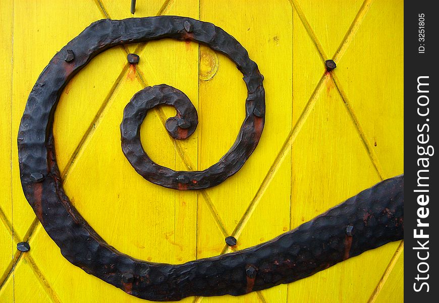 An Ornate Door Hinge on Yellow Door.