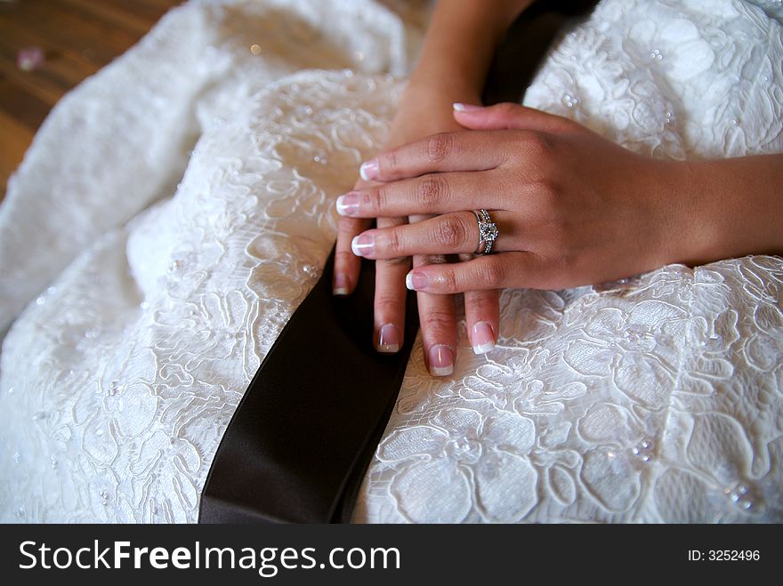 A new bride's hands resting in her lap. The focus is on the diamond. A new bride's hands resting in her lap. The focus is on the diamond.