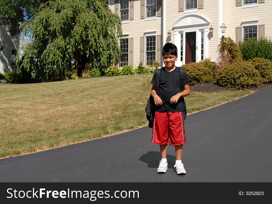 Elementary boy waiting for the school bus in front of his house.