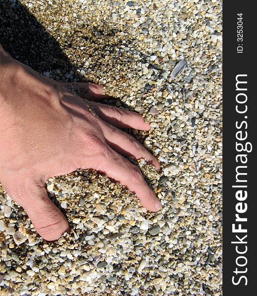A close up of a female hand merged in the pebbles at the beach