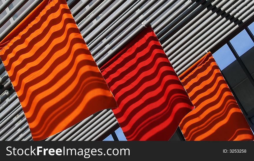 Ceiling's cross beams' shadows falling on bright red and orange flags creating a changing moving pattern on these flags