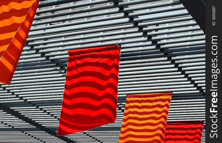 Ceiling's cross beams' shadows falling on bright red and orange flags creating a changing moving pattern on these flags