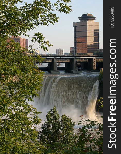 City skyling above Waterfalls.  Leafy green branches in the foreground. City skyling above Waterfalls.  Leafy green branches in the foreground.