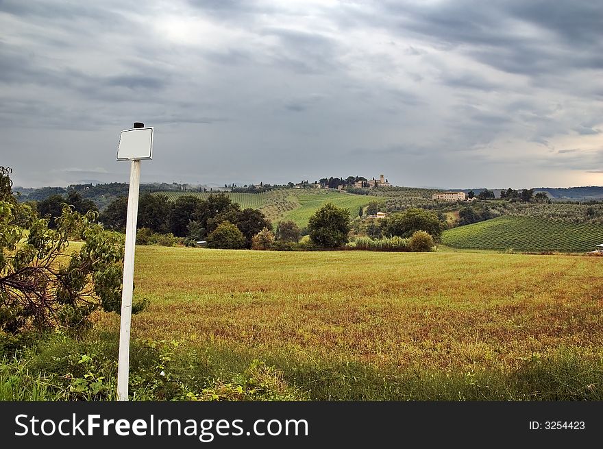 Pole with blank sign overlooking Tuscan hills with dramatic sky