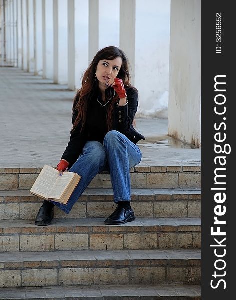 A girl sits on a stair with a book and holds glasses. A girl sits on a stair with a book and holds glasses