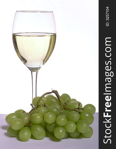 A glass of white wine and grapes, on white. A glass of white wine and grapes, on white