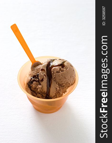 Two scoops of chocolate icecream in a orange plastic contain with a funny spoon
