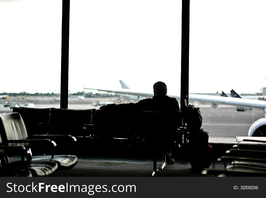 Man facing away from camera seated in airport lounge looking out the windows. planes visible through windows. Man facing away from camera seated in airport lounge looking out the windows. planes visible through windows.
