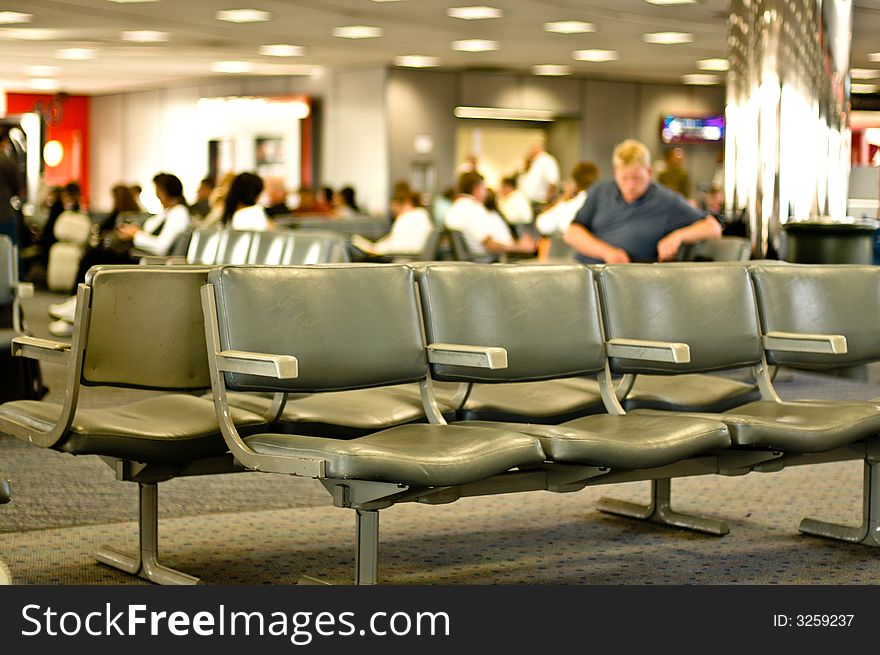 View of an airport lounge - people out of focus - waiting for their planes. empty row of seating in foreground, in focus. View of an airport lounge - people out of focus - waiting for their planes. empty row of seating in foreground, in focus