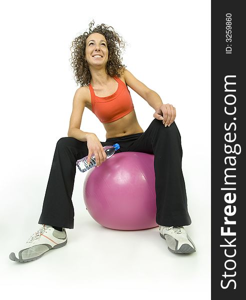 Young, beautiful woman sitting on big pink ball. Smiling and looking at something. Holding bottle of water. White background, low angle view. Young, beautiful woman sitting on big pink ball. Smiling and looking at something. Holding bottle of water. White background, low angle view