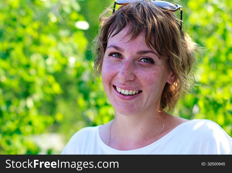 Young girl with freckles smiles on the background of green leaves. Young girl with freckles smiles on the background of green leaves