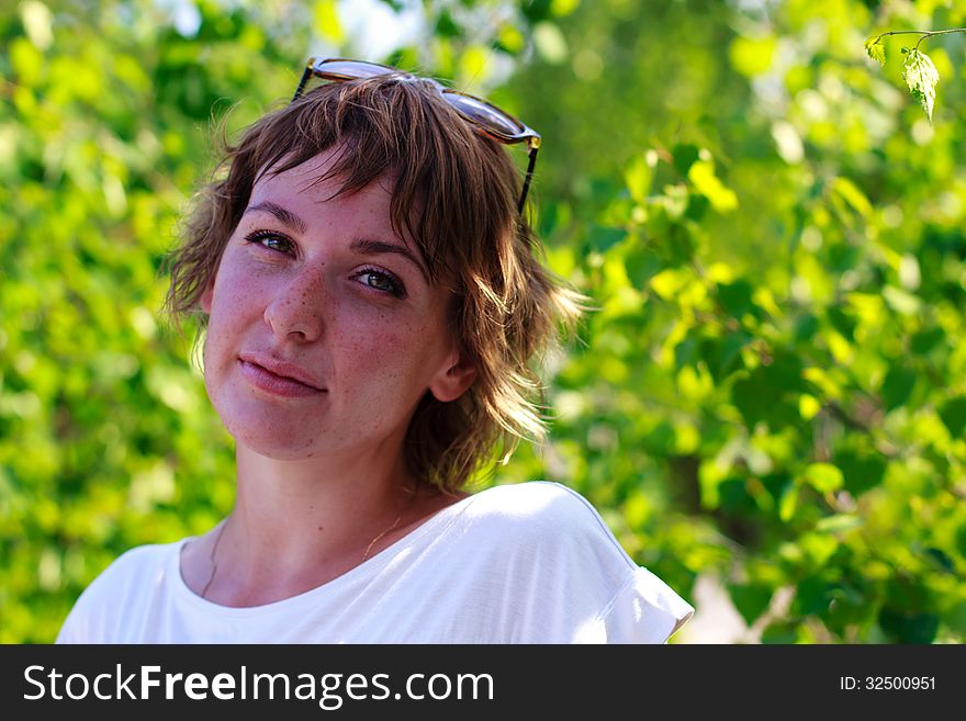 Young girl with freckles on the background of green leaves. Young girl with freckles on the background of green leaves