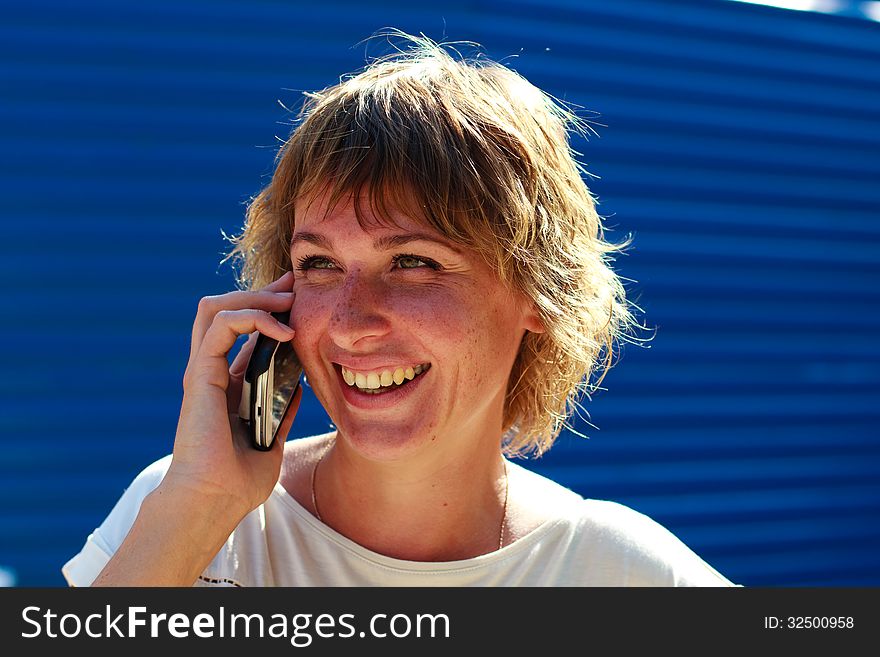 The girl smiling talking on the phone over blue striped background. The girl smiling talking on the phone over blue striped background