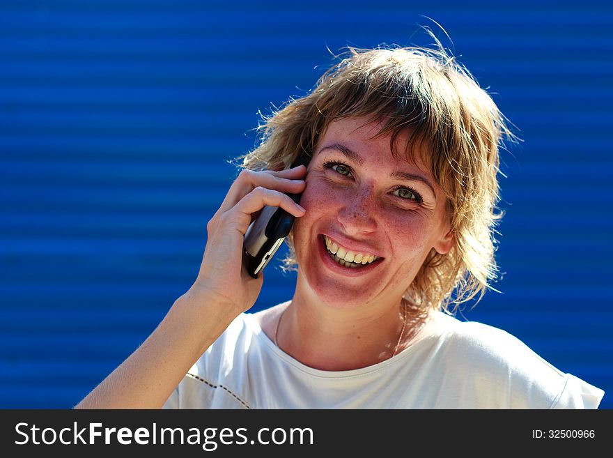 The girl smiling talking on the phone over blue striped background. The girl smiling talking on the phone over blue striped background