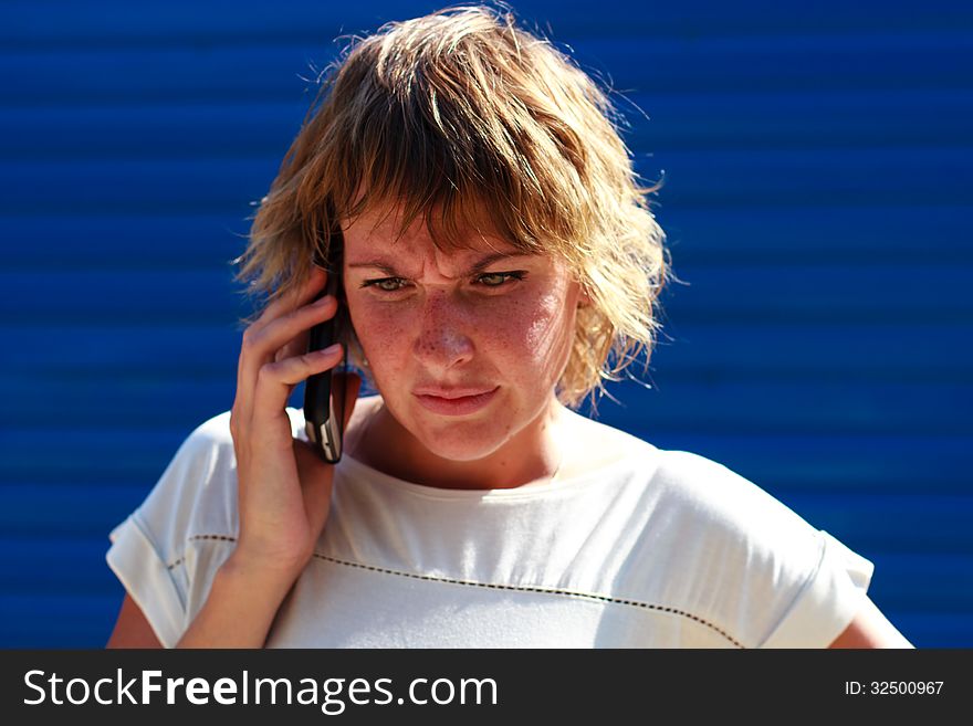 The girl got angry talking on the phone over blue striped background. The girl got angry talking on the phone over blue striped background