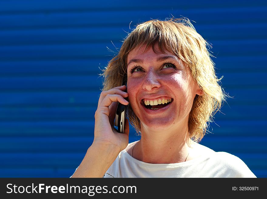 The girl smiling talking on the phone over blue striped background. The girl smiling talking on the phone over blue striped background