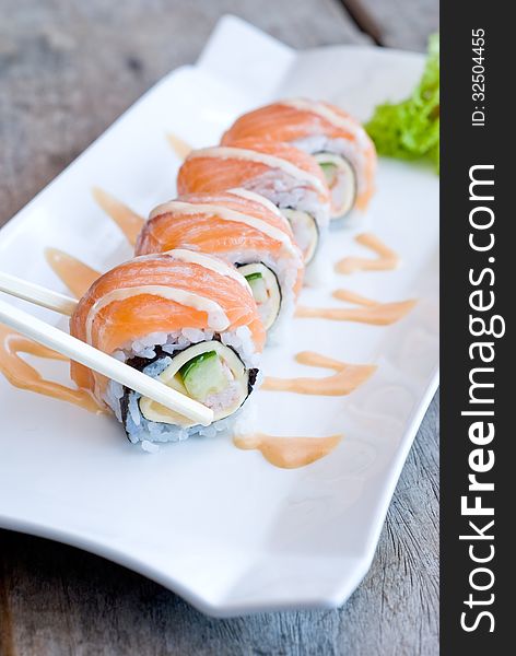 Using chopsticks with salmon sashimi roll on white plate topping with cream sauce