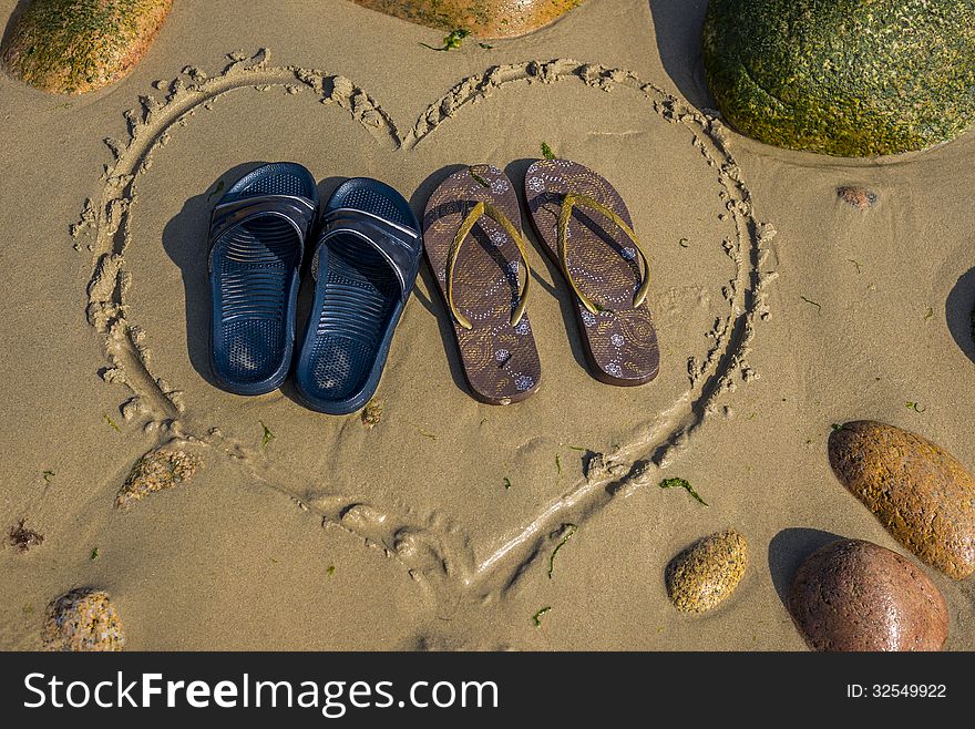A pair of male and a pair of female footwear standing in heart shape on the beach. A pair of male and a pair of female footwear standing in heart shape on the beach