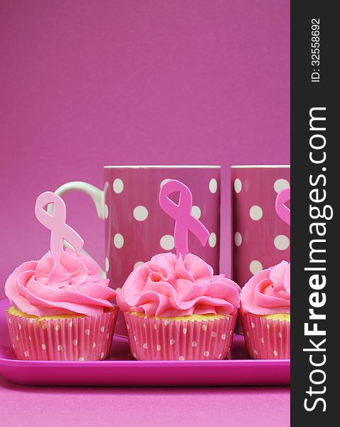 Pink cupcakes with Pink Ribbon symbol for International Breast Cancer Awareness charity month of October. with pink polka dot coffee mugs - vertical with copy space. Pink cupcakes with Pink Ribbon symbol for International Breast Cancer Awareness charity month of October. with pink polka dot coffee mugs - vertical with copy space.