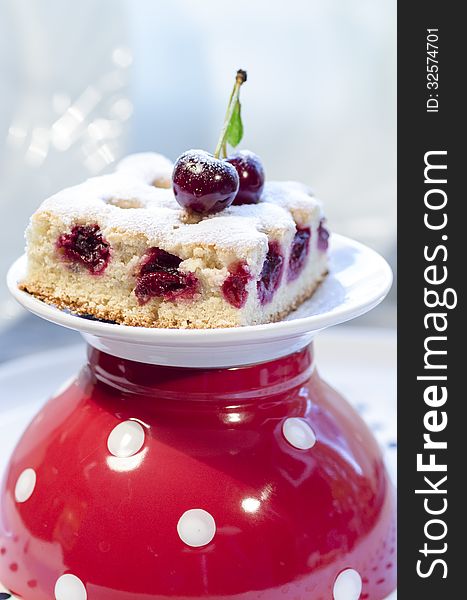 A slice of cherry pie on a linen napkin with polka dots. A cake decorated with fresh cherries. Next to a glass of juice. From the series Homemade Cherry Pie. A slice of cherry pie on a linen napkin with polka dots. A cake decorated with fresh cherries. Next to a glass of juice. From the series Homemade Cherry Pie