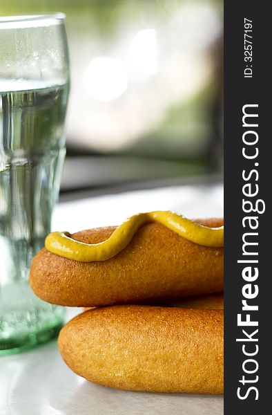 Close-up of corn dogs with mustard on with a drink in the background